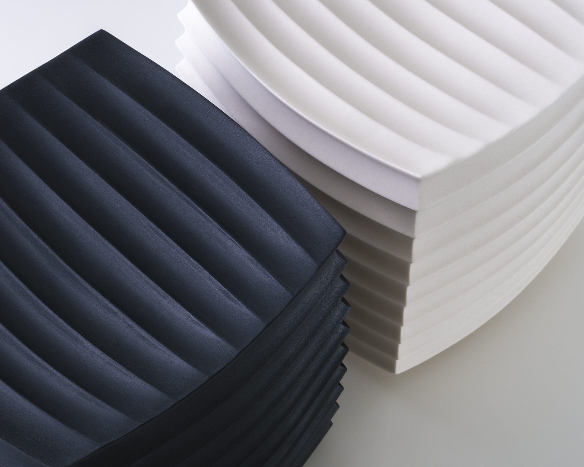 two abstract porcelain sculptures, one white and one black, loosely resembling intricately folded paper