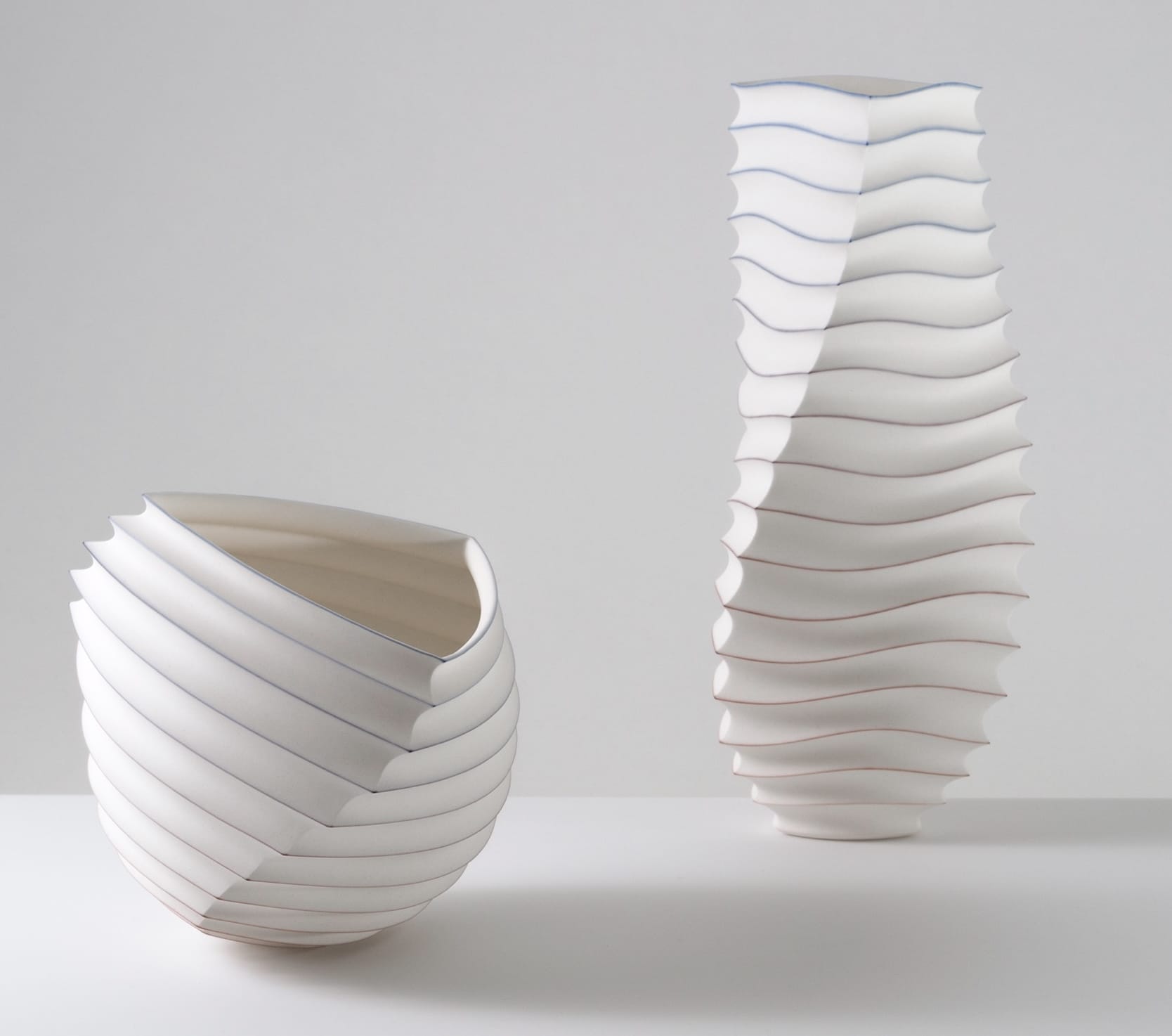 two abstract, white porcelain vessel sculptures loosely resembling intricately folded paper