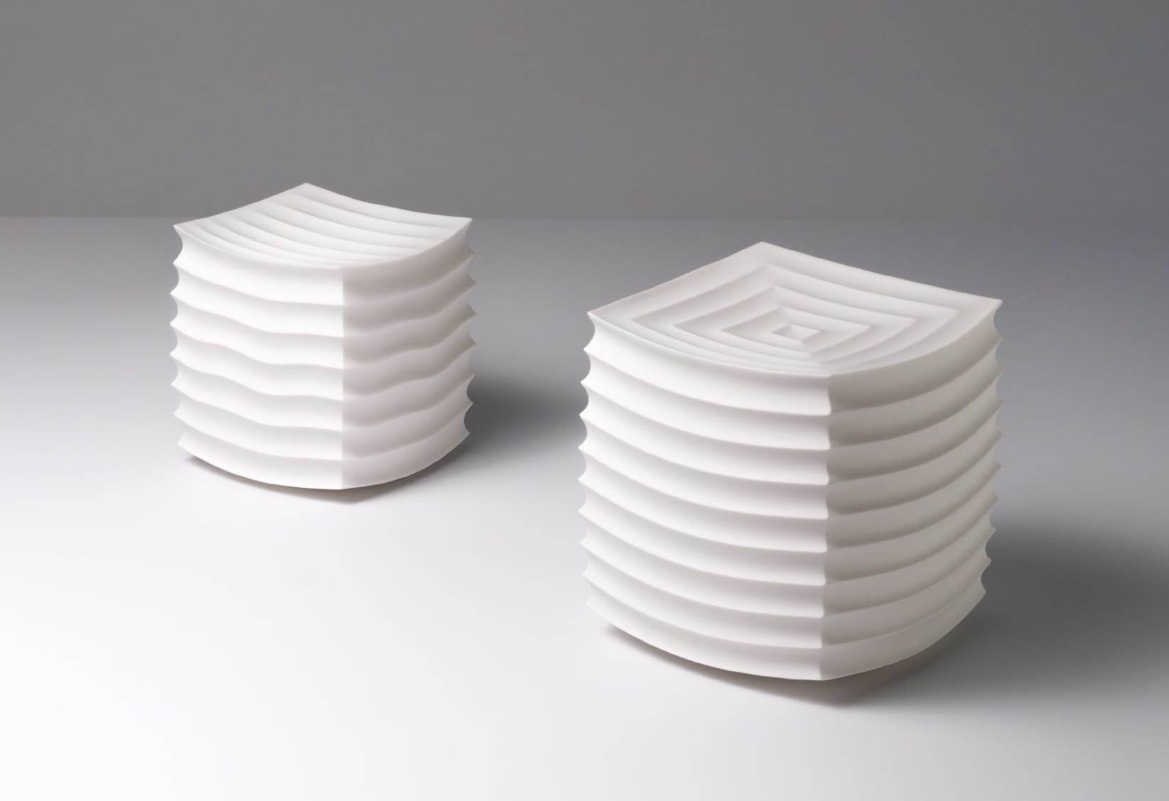 two abstract, white porcelain sculptures loosely resembling intricately folded paper