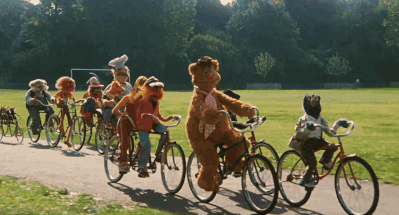 a gif of Muppets riding bikes through a park