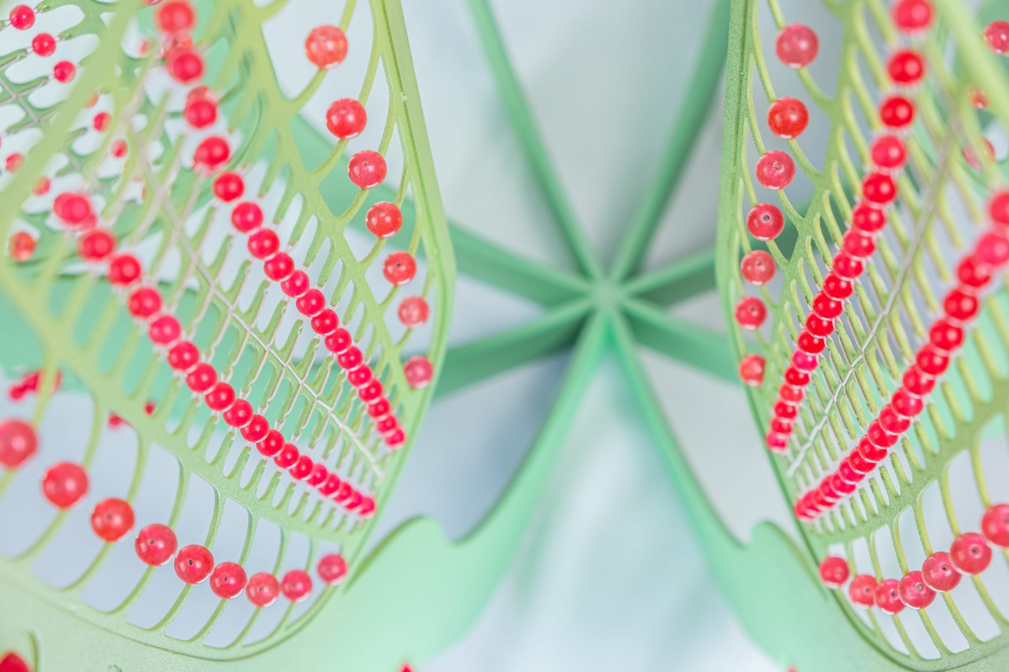 detail of a tall green curved sculpture with red beads on the sides
