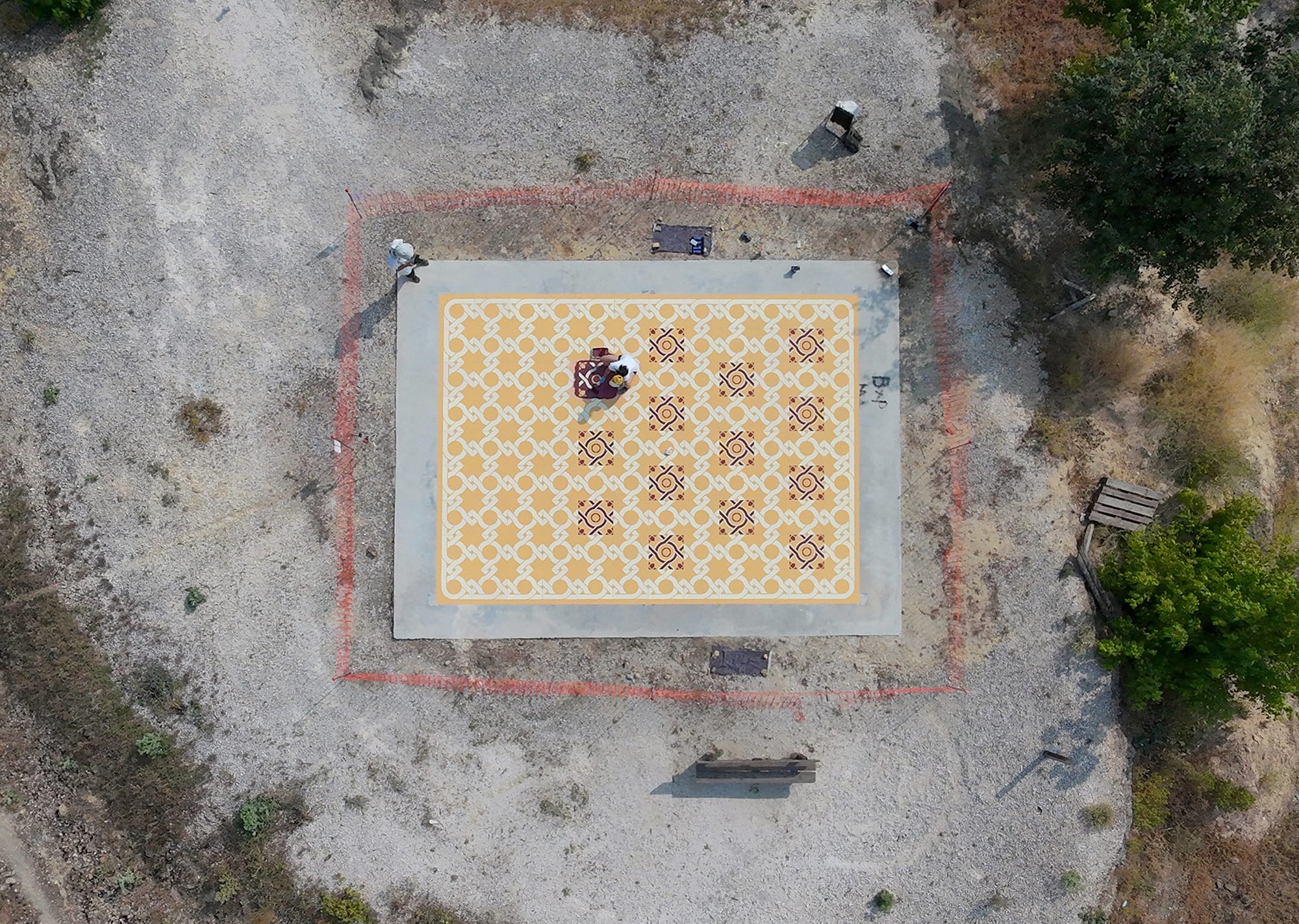an aerial view of an artist working on a red and yellow patterned rug in a vineyard