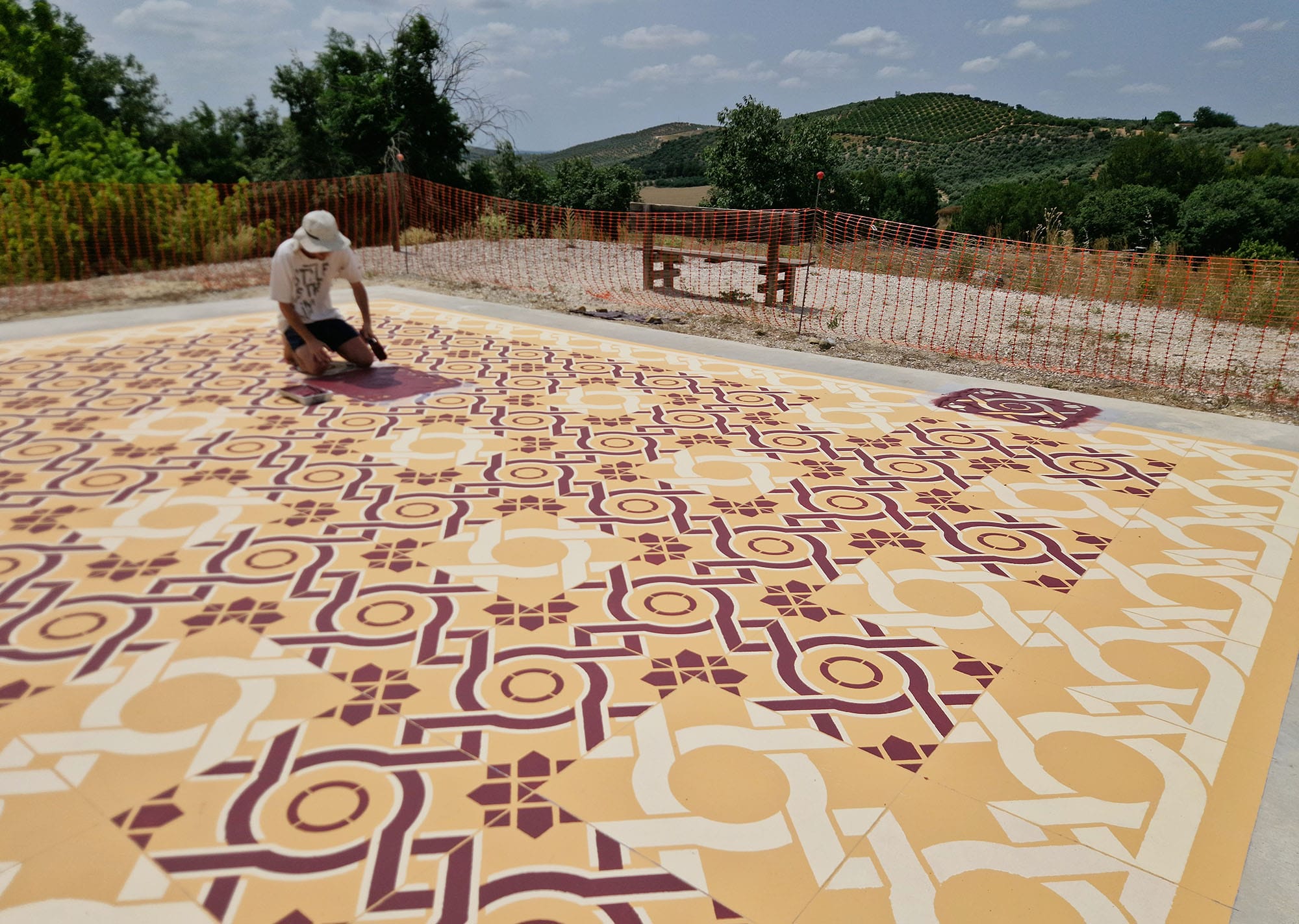 an artist working on a red and yellow patterned rug in a vineyard