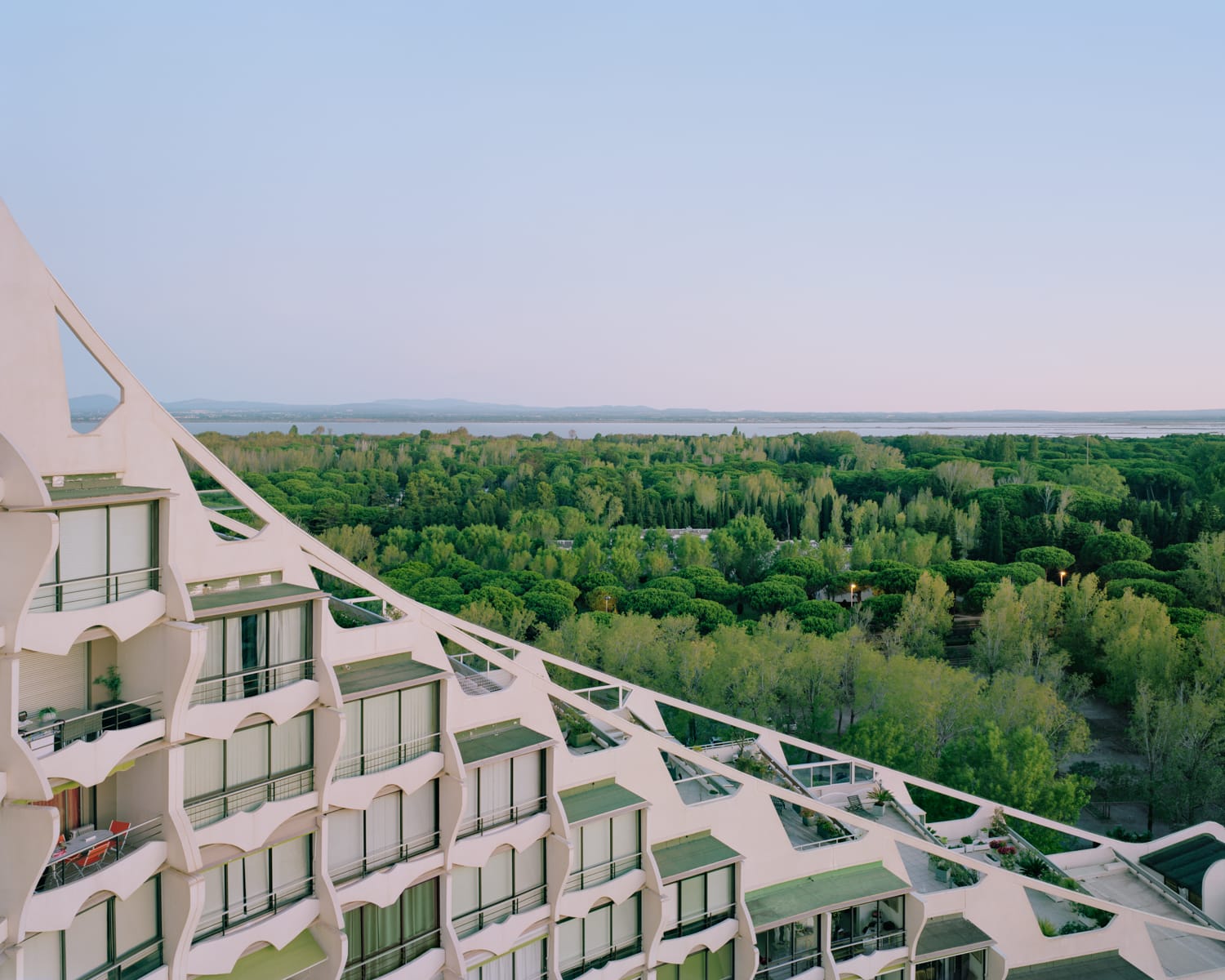 a detail of a modernist resort apartment complex in all-white against a blue sky near a broad, flat, green landscape