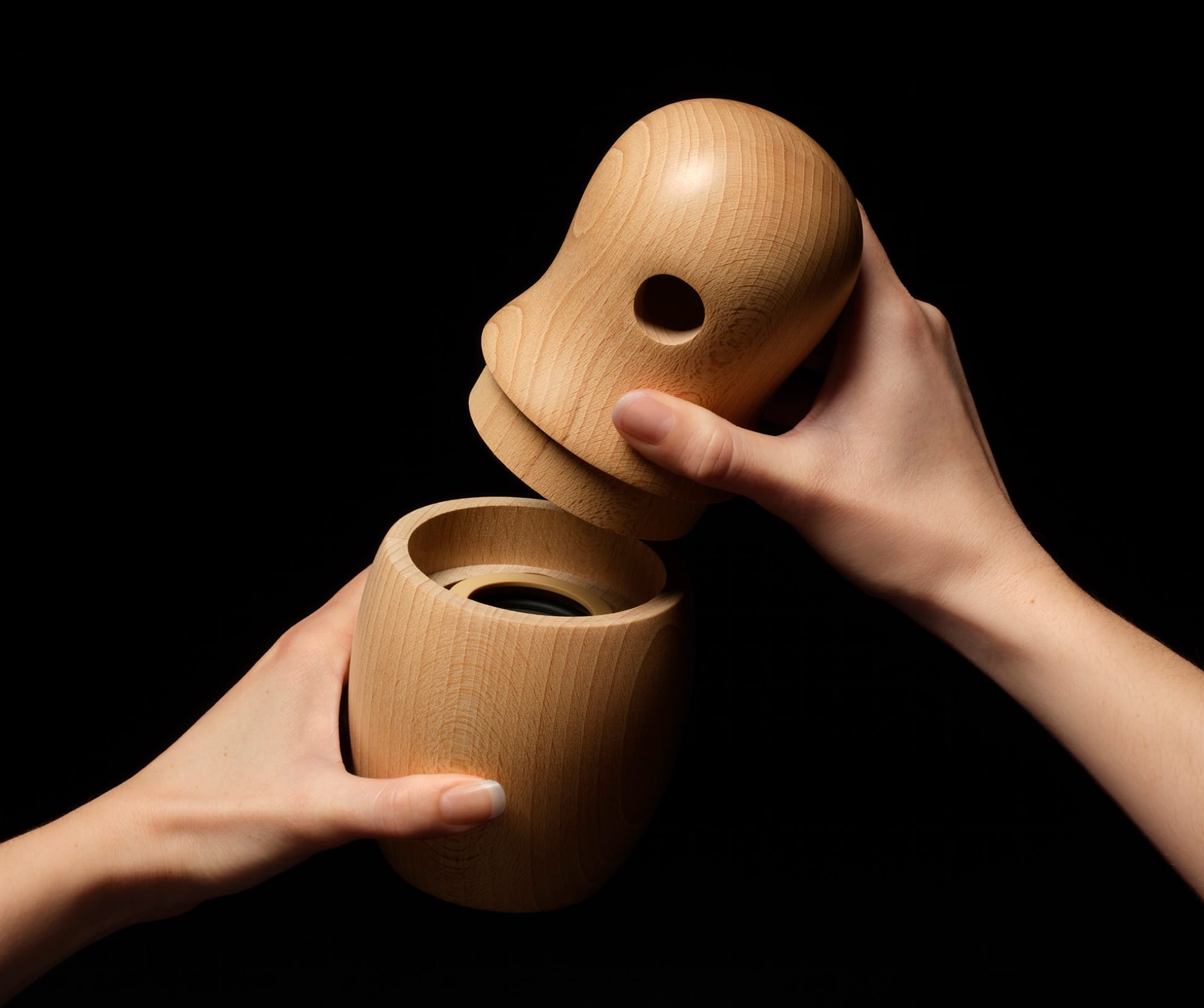 a wooden doll-like form with a speaker inside, held in two parts by two hands