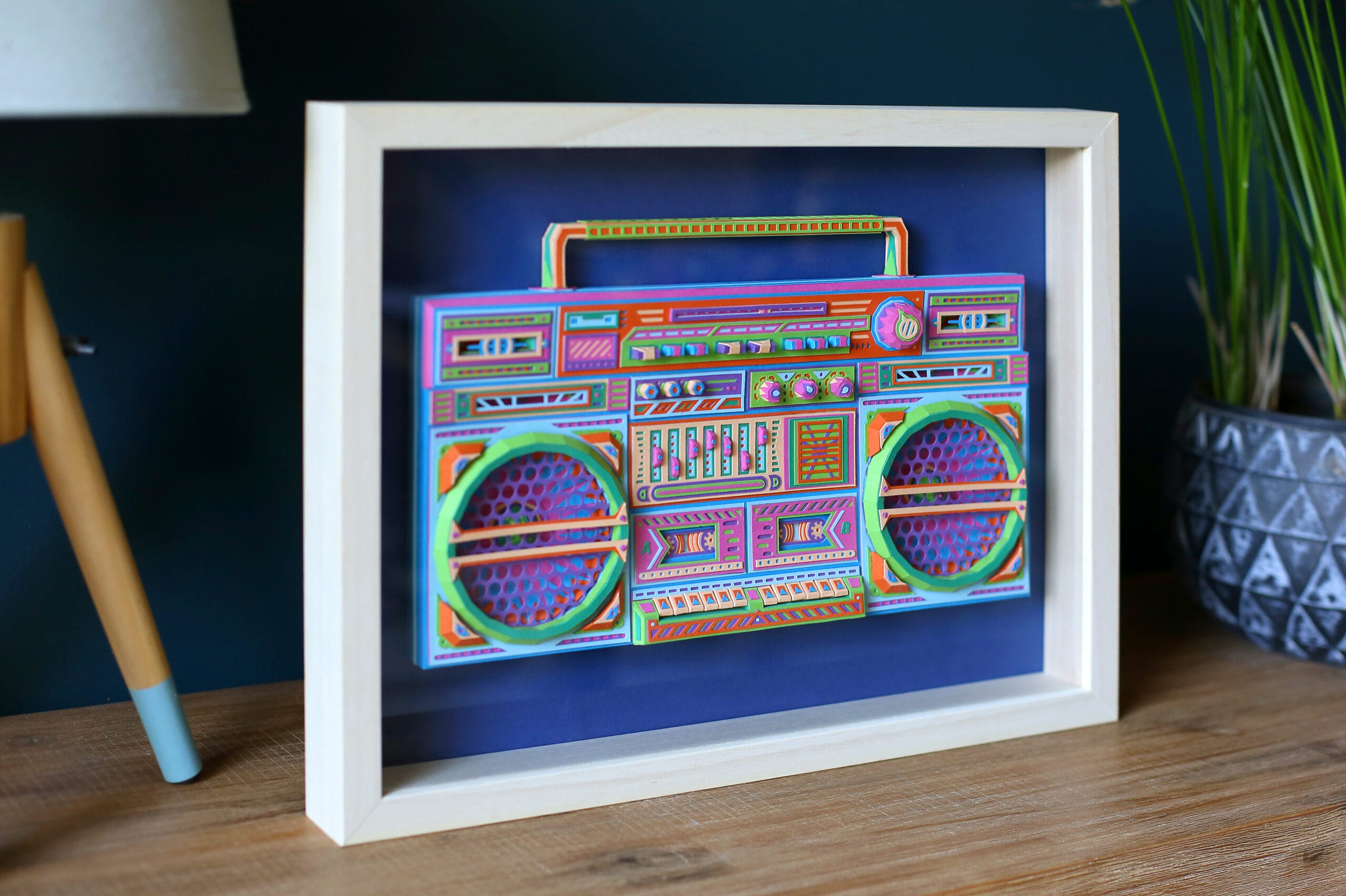 a colorful boombox made from paper, in a white frame