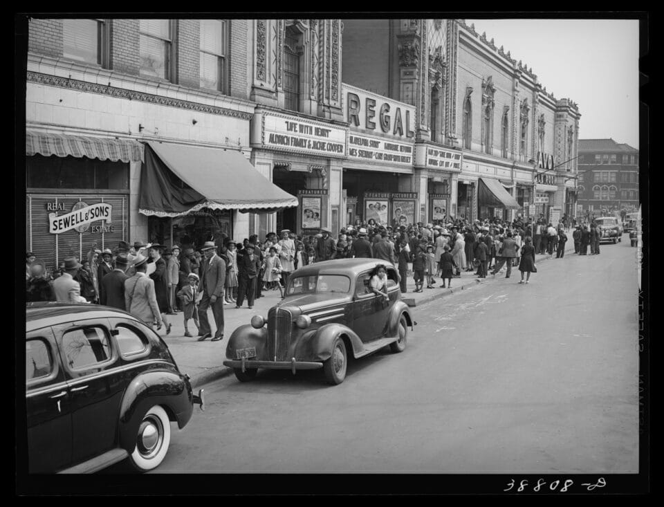 a black and white photo of people lining up outside a theater