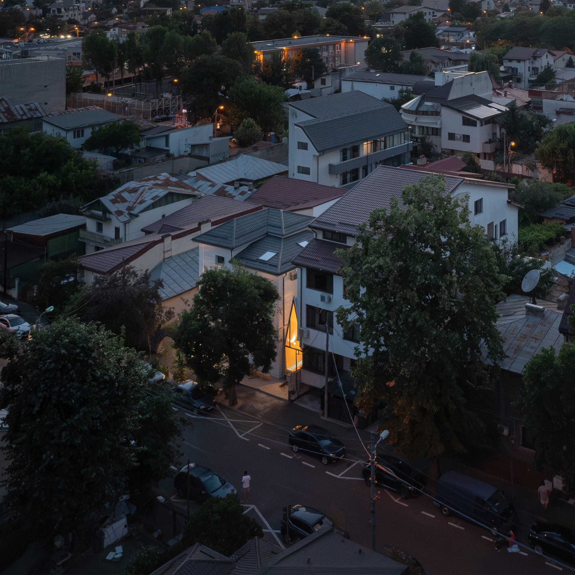 a tiny, contemporary cafe with a steep, pointed roof sits between two larger conventional buildings, designed by Vinklu and seen from the air
