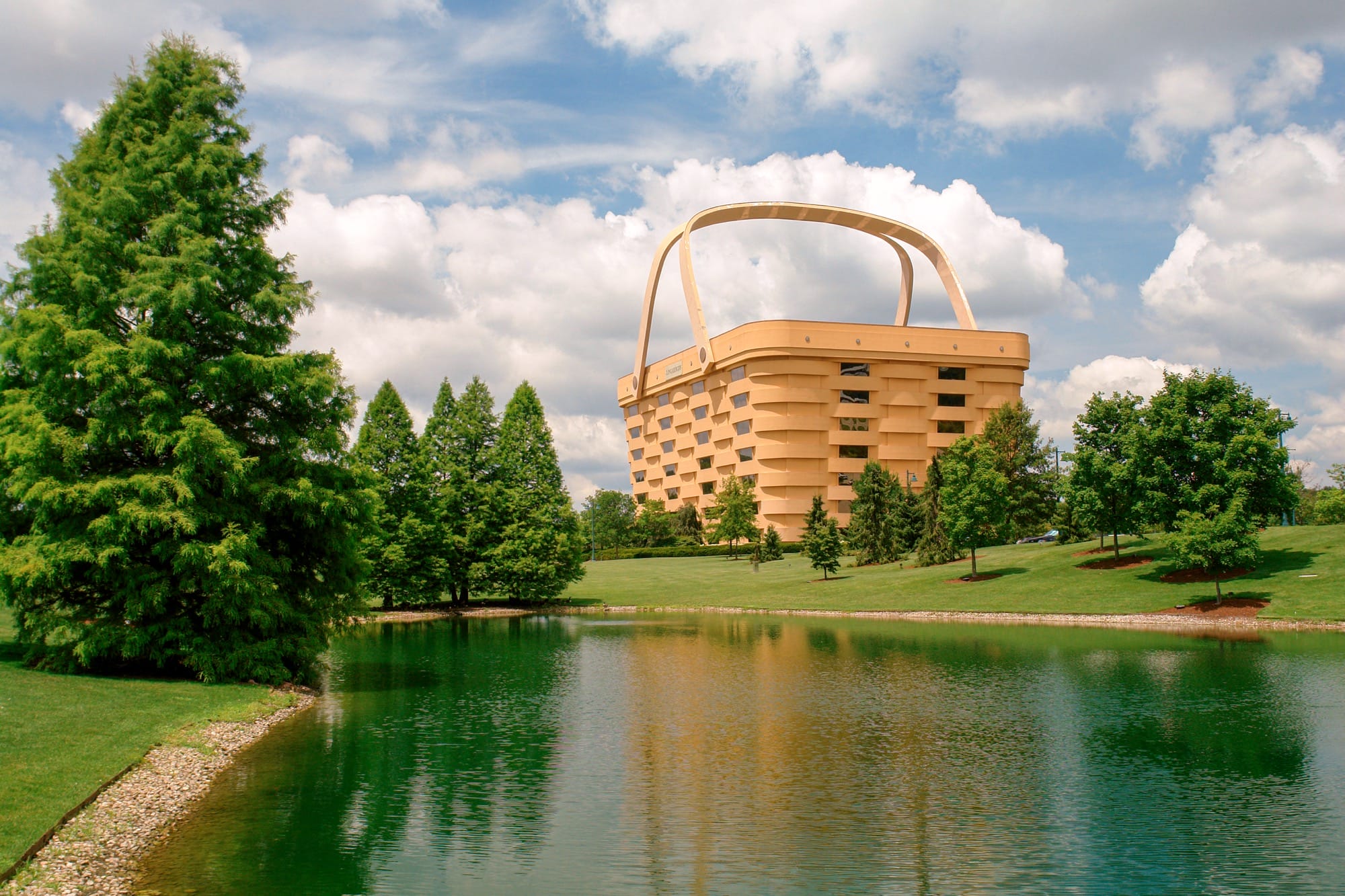 a building foregrounded by a pond, shaped like a giant picnic basket