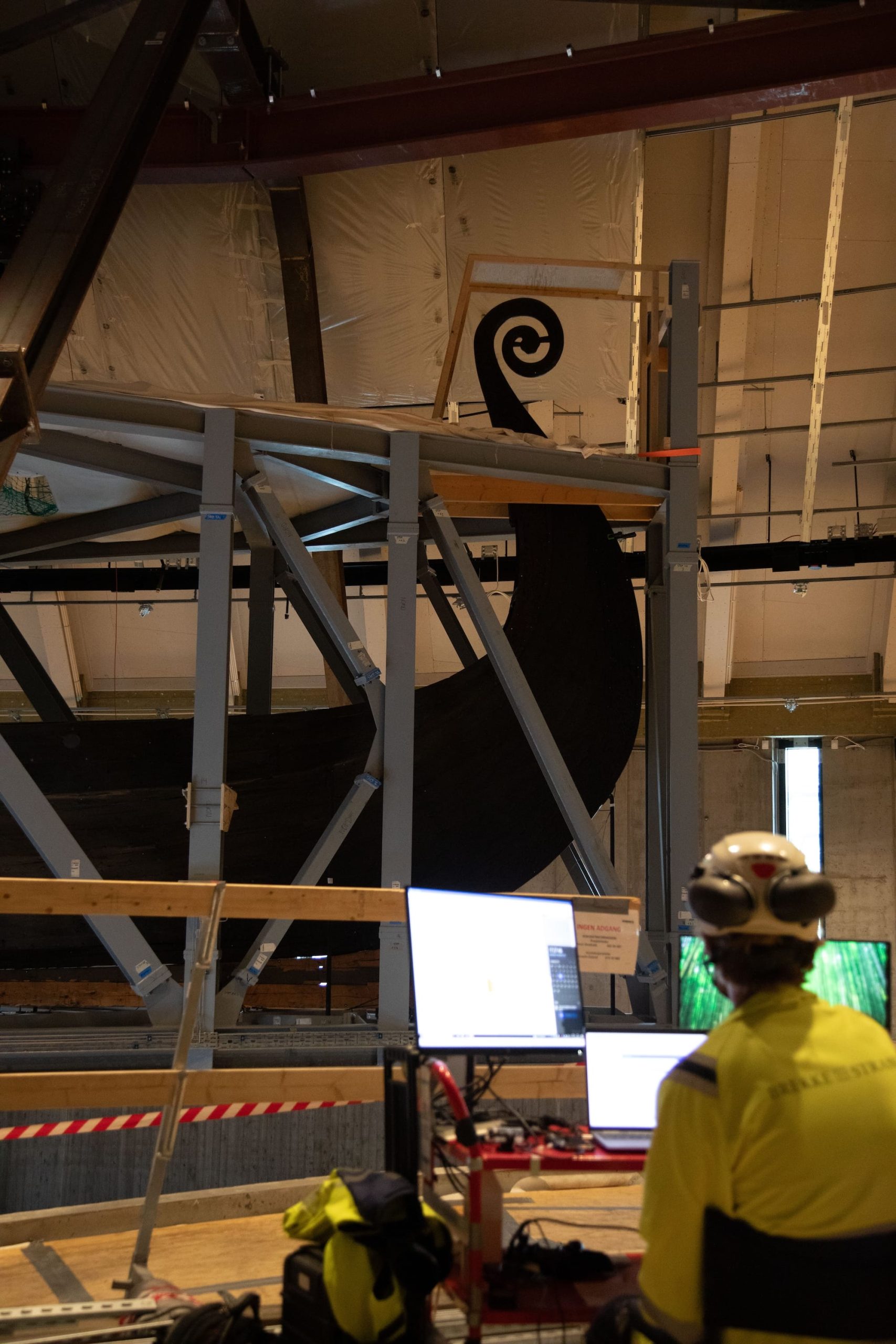 a researcher in hi-vis works in front of the Oseberg Viking Ship as it's moved through a museum in a huge steel crate