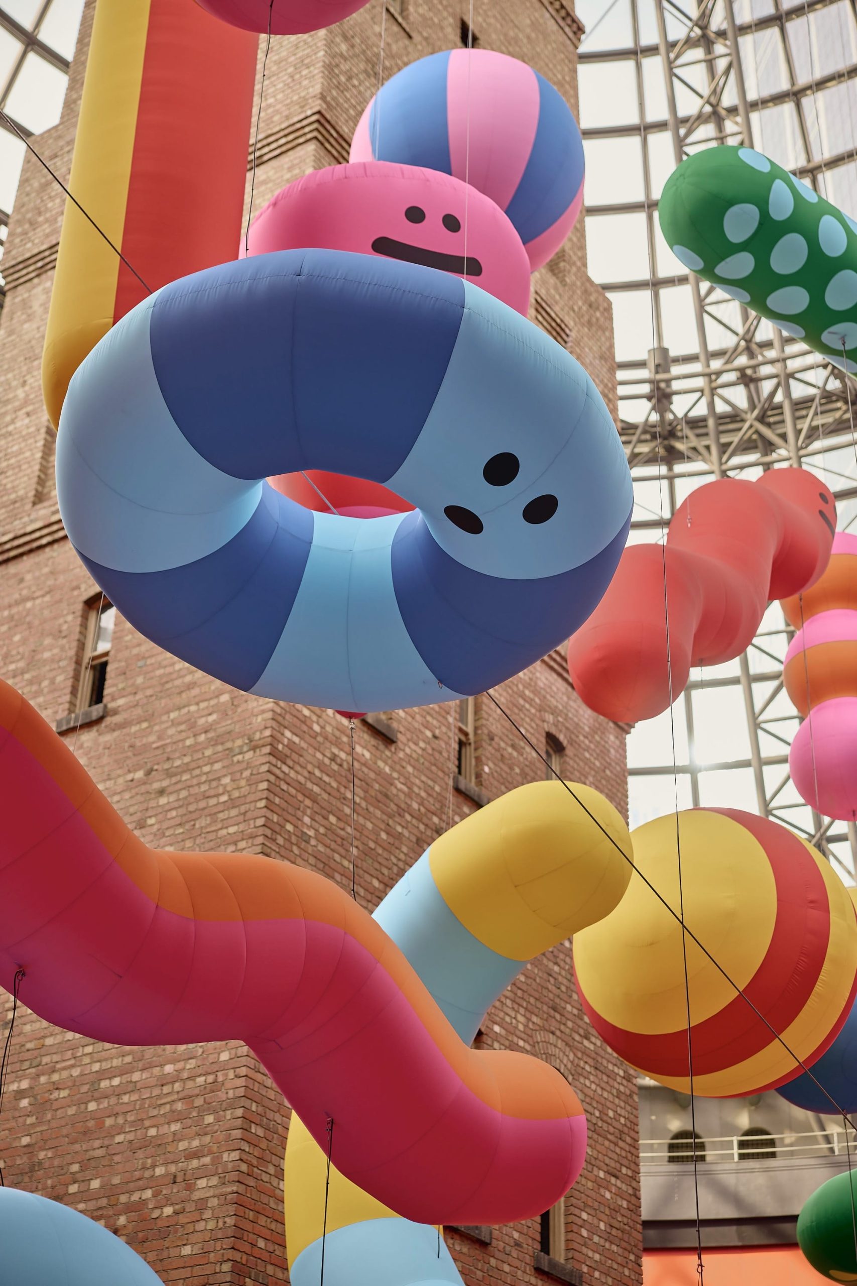 a detail of a large-scale installation in Melbourne Central of a number of abstract, colorful shapes, with expressive faces, suspended from the ceiling