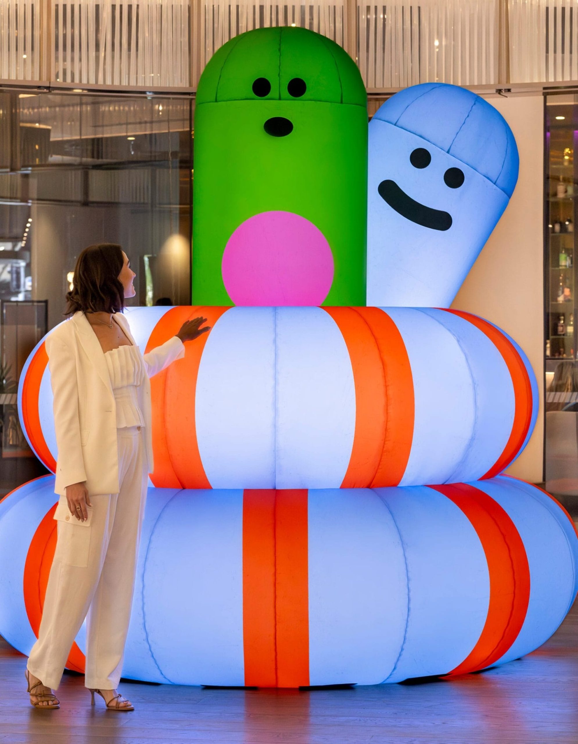 a woman stands in front of an inflatable sculpture by Craig & Karl of abstract, worm-like forms with smiley faces
