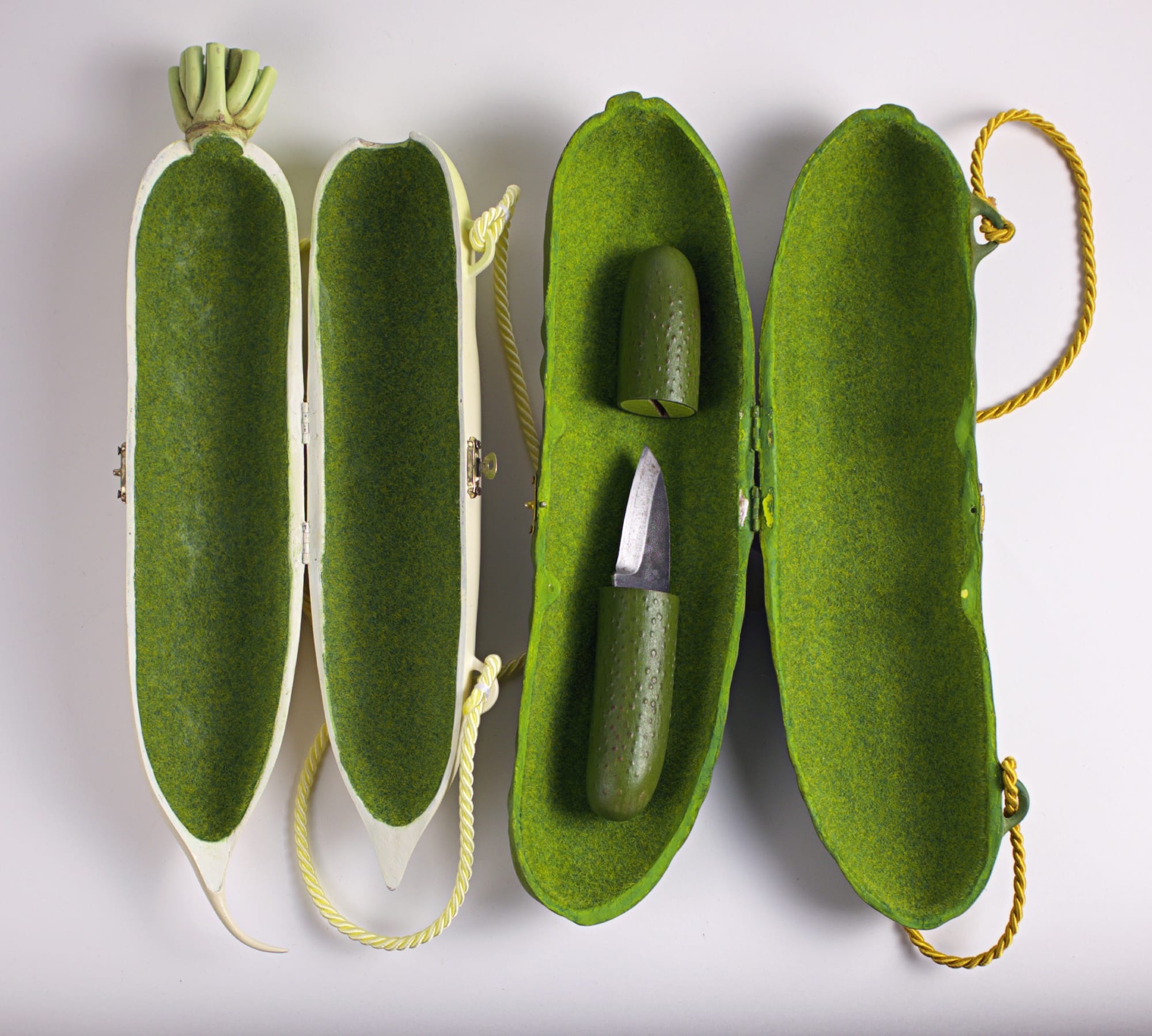 two sculptural purses by Paolo Puck shaped like a radish and a pickle, shown open, with the pickle purse containing a knife that is also shaped like a pickle