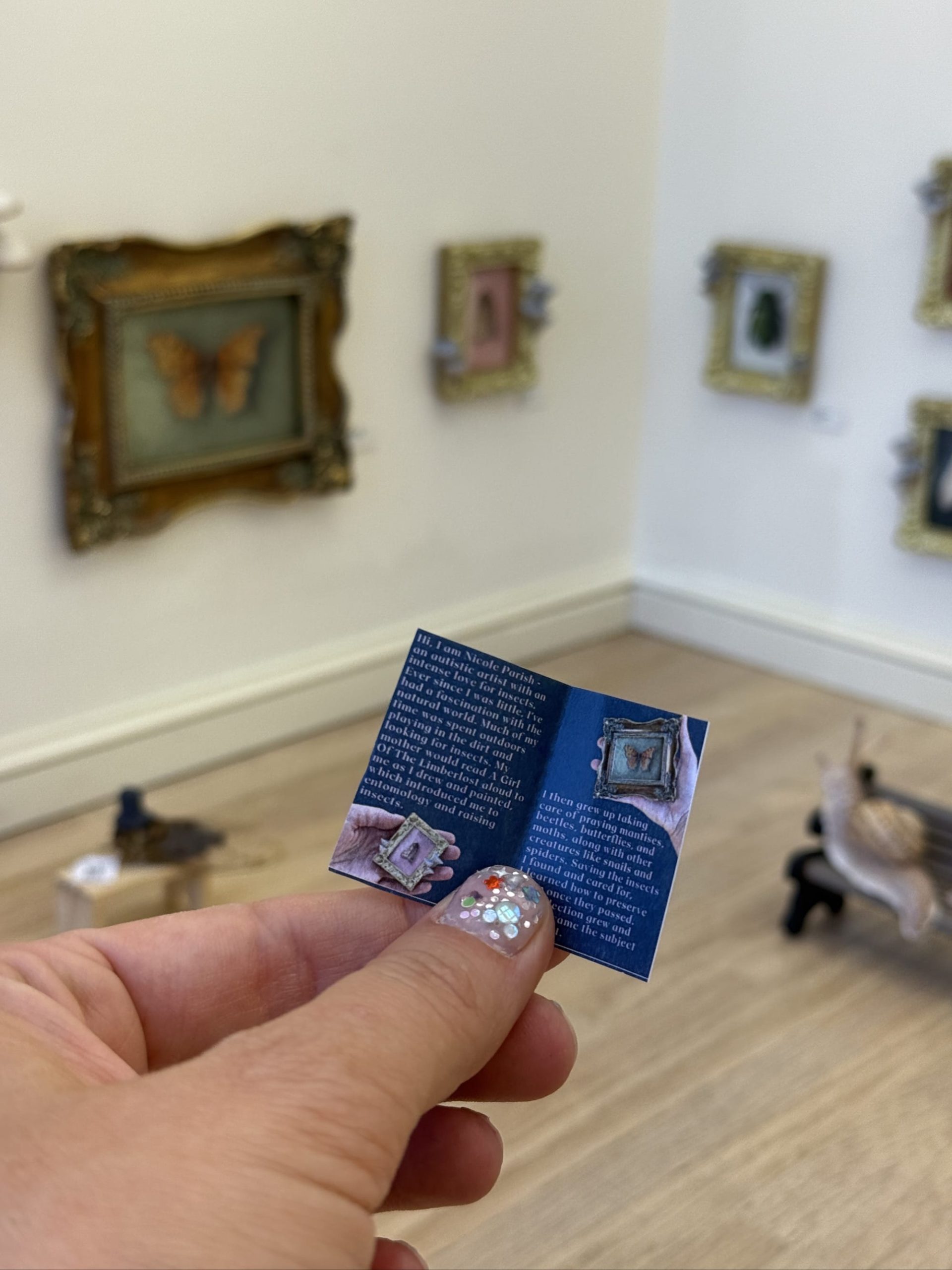 a hand holds a tiny brochure inside of a 1/6-scale gallery