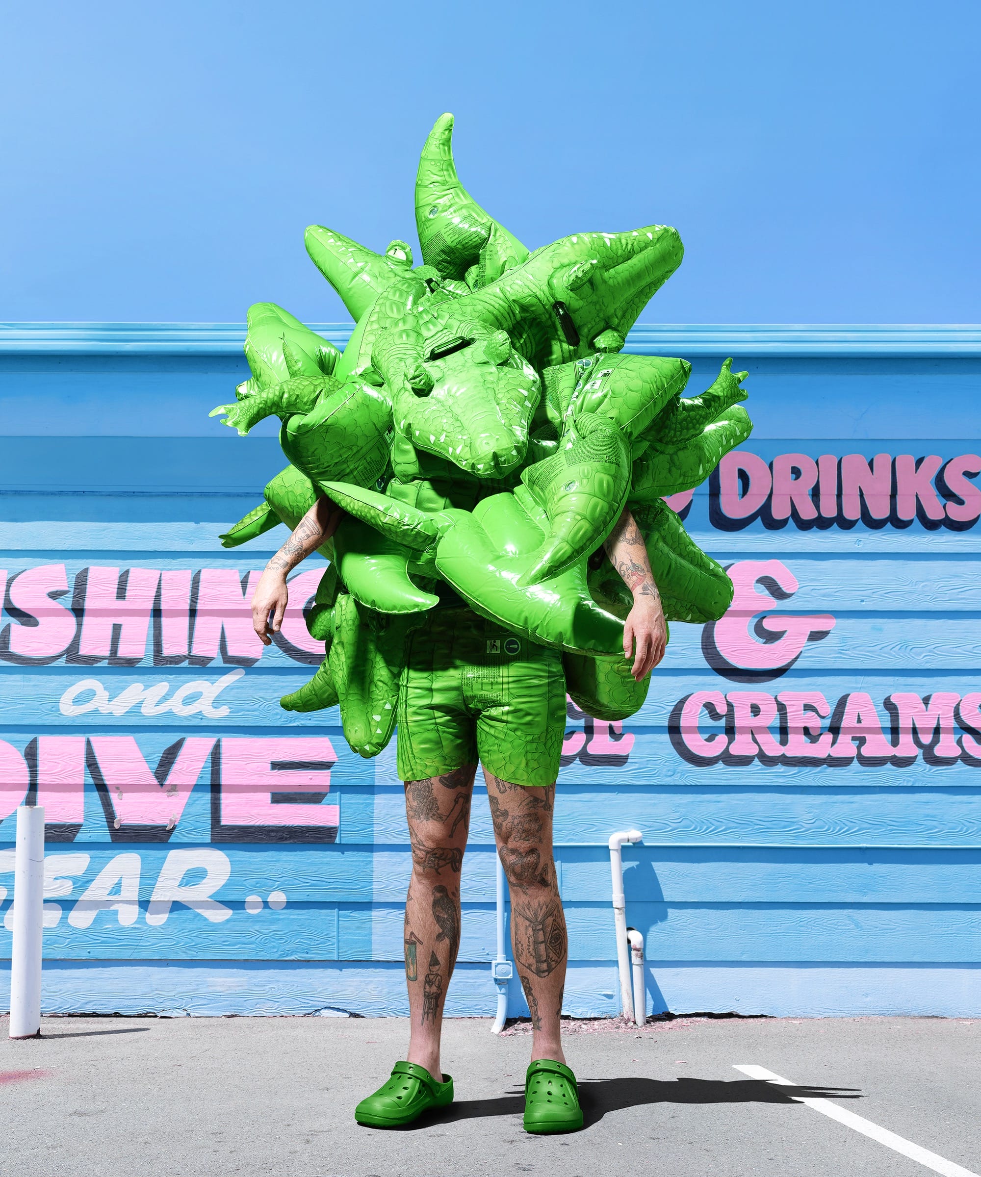 a photograph by Gerwyn Davies of a brightly colored abstract costume obscuring the top half of his body in front of a brightly painted building